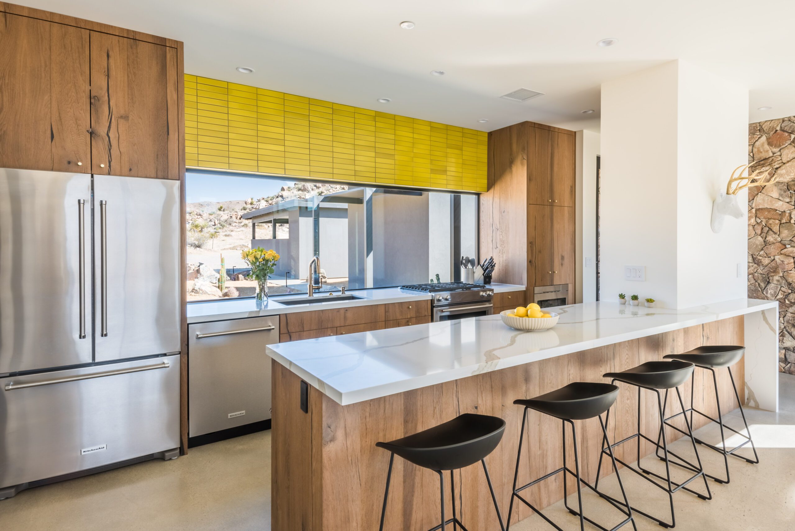 Modern kitchen interior with wooden cabinetry, stainless steel appliances, and a breakfast bar with stools.